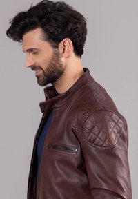 Brown leather jacket featuring quilted shoulder accents, a zippered chest pocket, and a collared neck design, smooth texture, and fitted shape.