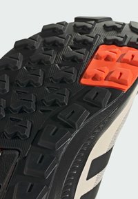 Czarna gumowa podeszwa do sneakersów z głębokim bieżnikiem dla lepszej przyczepności, z wyraźnymi czerwonymi i pomarańczowymi akcentami oraz fakturowanymi wzorami.