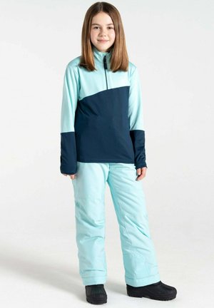 Hellblaue und marineblaue zweifarbige Winterjacke mit hohem Kragen, kombiniert mit passenden hellblauen Hosen und schwarzen Schneestiefeln.