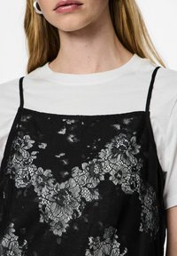 Melna mežģīņu kleita ar ziedu rakstu pārvalku, valkāta virs baltas T-krekla. Aprīkota ar plānām lencēm un mīkstu tekstūru.