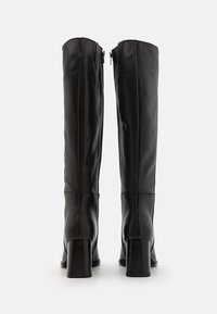 Paire de bottes en cuir noir montant jusqu'aux genoux, à talons blocs, vues de dos sur fond blanc.