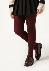Burgundy strumpbyxor kombinerat med glansiga burgundy loafers. En svart plisserad kjol fulländar outfiten, tillsammans med en vit tröja med marinblå ränder.