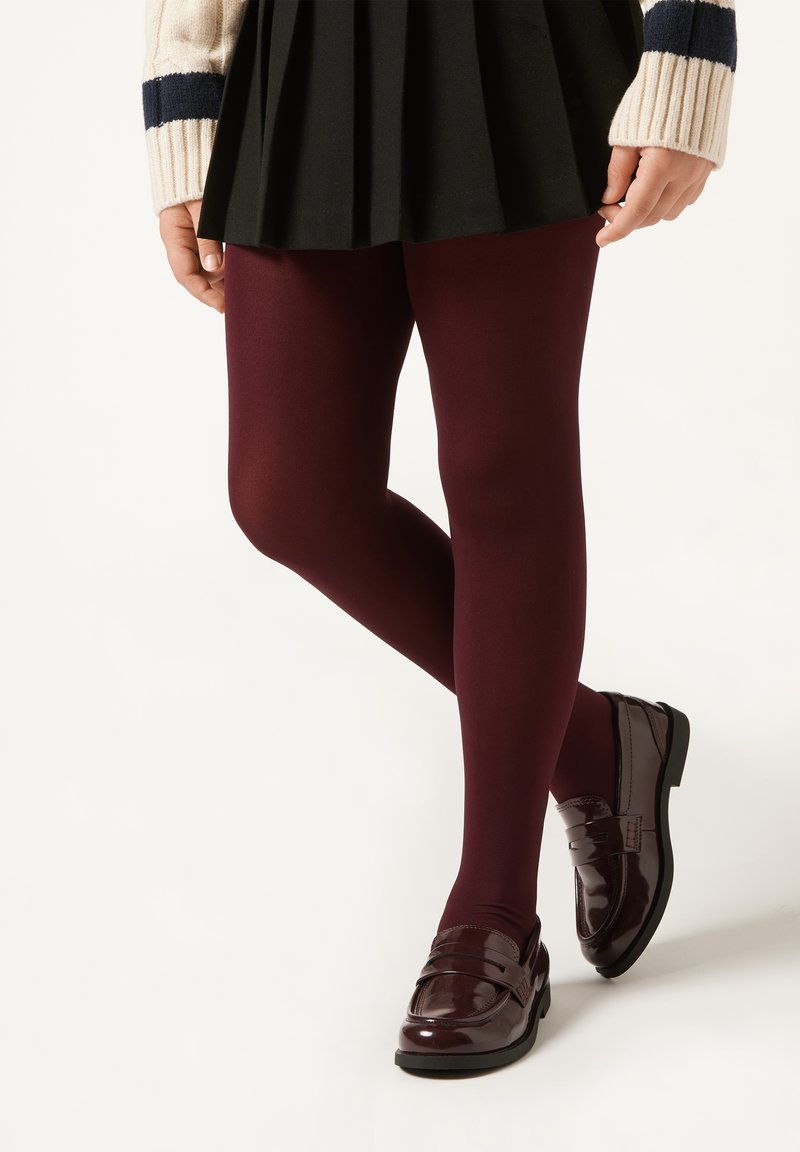 Burgundy strumpbyxor kombinerat med glansiga burgundy loafers. En svart plisserad kjol fulländar outfiten, tillsammans med en vit tröja med marinblå ränder.