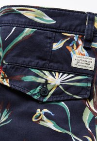 Țesătură bleumarin cu un model floral multicolor. Are un tiv cusut, închidere cu buton și un eticheta care spune "Levi Strauss."