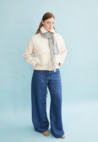 Cream wool-blend jacket with two front pockets, paired with light blue denim wide-leg pants and a light gray scarf. Smooth textures throughout.