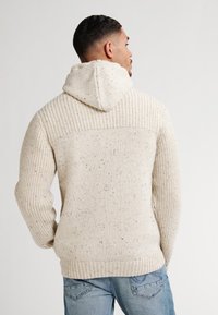 Maglione con cappuccio in off-white con un design a coste testurizzato. Presenta un motivo maculato e una vestibilità rilassata con fondo orlato.