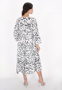 Leopardprint maxi kjole med lagdelt design, hvid baggrund, sorte mønstre, lange ærmer og rund halsudskæring. Sølvfarvede stiletter med stropper.