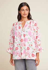 Blomstret bluse med V-hals, prydet med rosa, røde og grønne blomster på en hvit bakgrunn. Lange, puffete ermer med rynkede mansjetter.