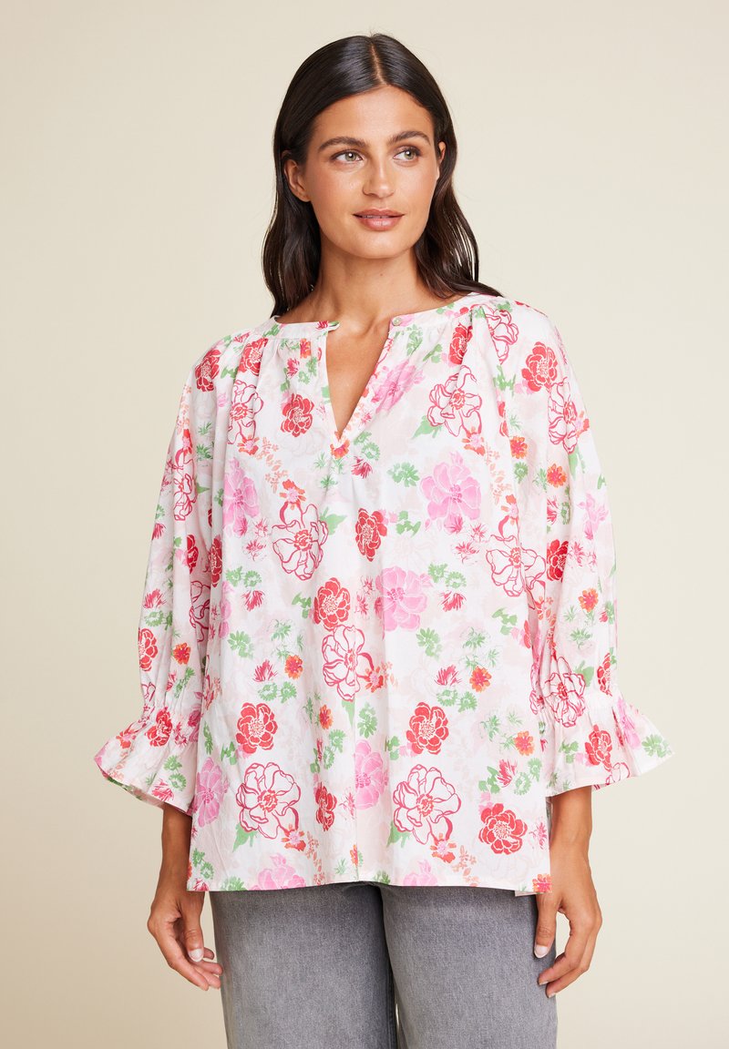 Blomstret bluse med V-hals, prydet med rosa, røde og grønne blomster på en hvit bakgrunn. Lange, puffete ermer med rynkede mansjetter.