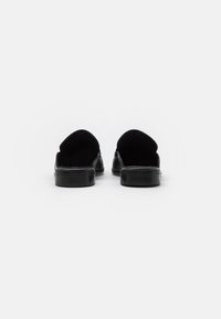 Fekete bőr slip-on cipők texturált felülettel és kerek háttal. Simább talp és belső rész; minimalista dizájn, alkalmas hétköznapi viseletre.