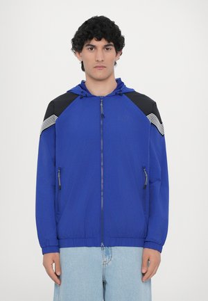 Blue zip-up jacket with black shoulder accents and striped detailing. Features a hood, elastic cuffs, and side zip pockets. Smooth texture.