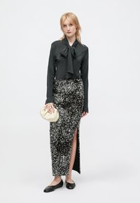 Czarna bluzka z kołnierzykiem w kształcie kokardy, zestawiona z cekinową spódnicą do kostek z wycięciem na udzie. Akcesoria to beżowy kopertówka i płaskie buty.