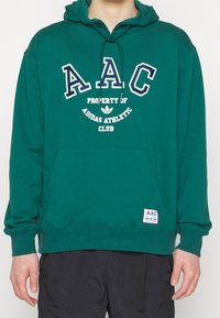 Grön huvtröja i bomullsblandning, med broderad "AAC" logotyp och Adidas grafik. Inkluderar en framficka och ribbade ärmslut.