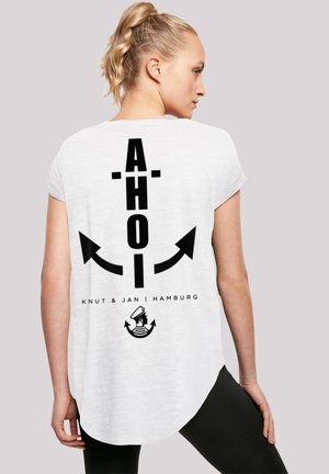 Weißes T-Shirt mit kurzen Ärmeln, das mit einem auffälligen schwarzen Schriftzug "AHOI" mit Pfeilen, dem Text "Knut & Jan | Hamburg" und einer Matrosengrafik am unteren Ende gestaltet ist.