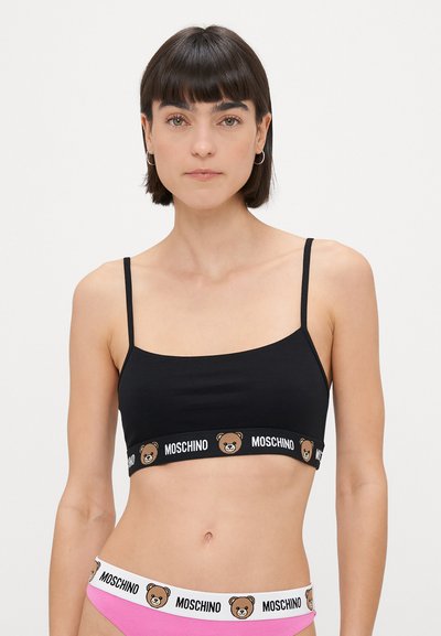 Melnas kokvilnas bralette ar plānām regulējamām siksnām, ar baltu jostu, kas rotāta ar lāča grafiku un "Moschino" tekstu.
