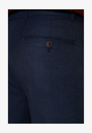 Granatowe spodni w kratę z tylną kieszenią zapinaną na brązowy guzik, wykonane z teksturowanego materiału dla dodatkowego efektu.