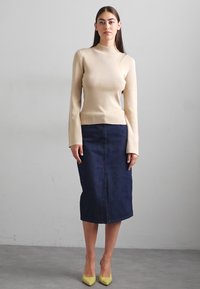 O bluză bej cu mânecă lungă, ajustată, asortată cu o fustă midi din denim închis și pantofi cu vârf pointat galbeni. Texturi netede și elemente de design minime.