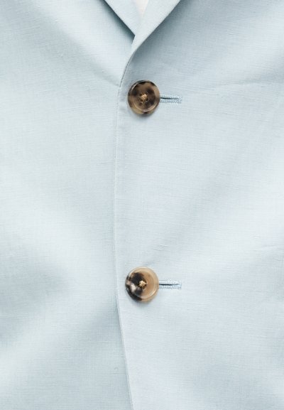 Ανοιχτό μπλε ύφασμα με δύο κουμπιά με σχέδιο χελώνας, στερεωμένα στο μπροστινό μέρος ενός σακακιού ή μπουφάν.