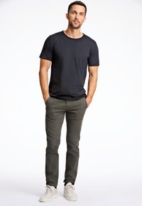 Svart crew-neck t-shirt kombinerad med olivgröna slim-fit byxor och vita sneakers. Slät tyg med avslappnad passform och minimalistisk design.