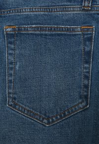 Zadní kapsa modrých džínů z denimu s oranžovým prošíváním a mírným opotřebením látky u levého horního rohu kapsy.