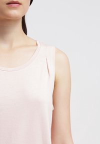 Top senza maniche di un rosa chiaro, con collo rotondo, realizzato in tessuto morbido, caratterizzato da un delicato dettaglio plissettato sulla spalla.