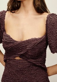 Haut texturé mauve avec des petites manches bouffantes, mettant en avant un design froissé et une coupe croisée, révélant une découpe à la taille.