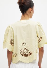 Gelbes Baumwolloberteil mit aufwendigen Spitzenverzierungen an den Ärmeln und dem Saum, mit floralen Mustern und gewellten Kanten. Leichter Stoff.