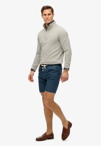 Pullover gris avec un col, shorts bleu marine avec cordon de serrage, et mocassins marron. Le pullover présente un design texturé.