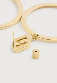 Guld hoop øreringe med en rektangulær charmerende vedhæng, der har et stiliseret tal fem og en lille cylindrisk bagside ved siden af dem.