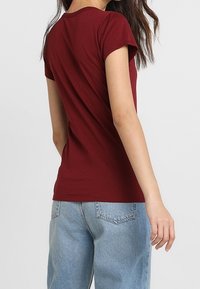 Burgundy kortärmad t-shirt med rund halsringning, mjukt bomullstyg, figurnära design och en enkel, sömlös baksida. Kombinerad med ljusblå jeans.