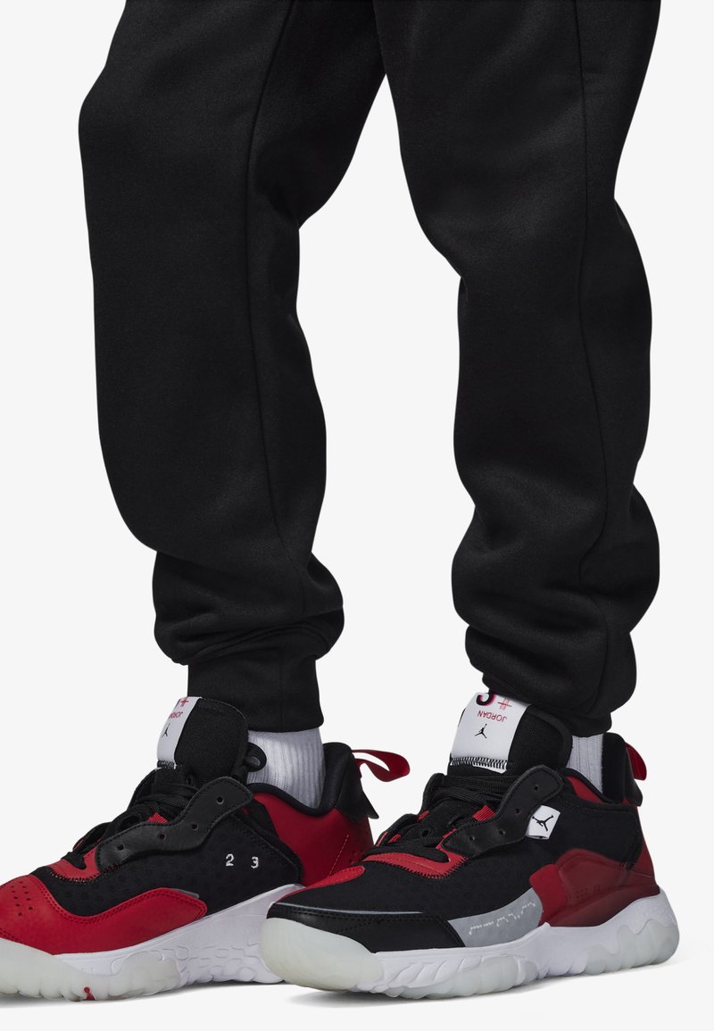 Baskets de sport noires et rouges avec un maillage texturé et des accents en cuir lisse, dotées d'une semelle blanche et d'un logo bien en vue sur la languette.
