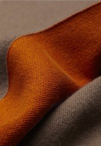 Ulltyg i nuanser av varm orange och mjuk grå, som visar upp en slät textur och subtila stickade mönster med mjuka veck.