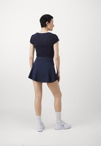 Navy fitted short-sleeve top paired with a flared navy skirt. Model is wearing white athletic shoes and knee-high white socks.