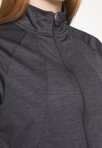 Grå sportig zip-up jacka med hög krage, subtil textur och framdragkedja. Har kontrasterande sömmar för ytterligare detalj.