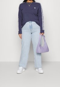 Námořnická košile s dlouhým rukávem a bílými pruhy, světlé modré džíny s vysokým pasem, bílé tenisky a malá kabelka s texturou krokodýlí v odstínu fialové.