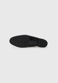Suola di scarpa nera con una texture liscia, punta arrotondata e motivo di battistrada minimale. Presenta il logo del brand impresso. Design elegante e piatto.