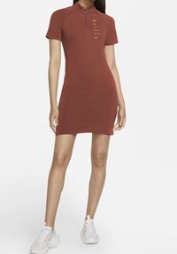 Czerwono-burgundowa sukienka Nike z krótkim rękawem i zamkiem przy kołnierzyku; zawiera slogany i logo w kolorze pomarańczowym. Gładka tekstura, dopasowany krój.