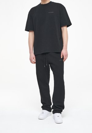 Czarna bawełniana koszulka z krótkim rękawem i okrągłym dekoltem, w zestawie z czarnymi spodniami dresowymi z bocznymi kieszeniami i sznurkiem w pasie.