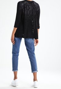 Black knitted top with geometric cut-out patterns, long sleeves, paired with light blue rolled-cuff jeans and white platform sneakers.