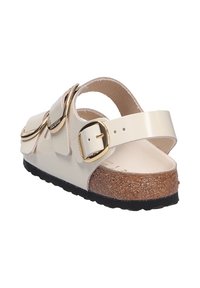 Sandali beige in vernice con dettagli in metallo dorato, cinturino regolabile, soletta in sughero e suola nera testurizzata. Presentano un dettaglio con doppia fibbia.
