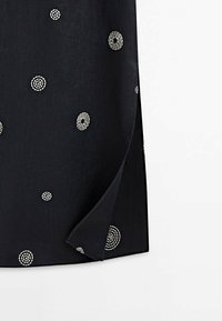 Tissu noir avec des motifs d9broderie circulaires blancs. Le dessin pre9sente des cercles concentriques de tailles varie9es et un ourlet partiel.