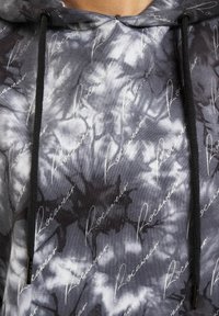 Hoodie grigia tie-dye con logo bianco a script ripetuto, cappuccio con coulisse e texture di tessuto morbido. Motivi sottili in tonalità più scure.