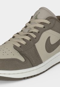 Χαμηλή μπεζ και καφέ δερμάτινη αθλητική παπούτσια με λευκά κορδόνια, διάτρητο μπροστινό μέρος και το λογότυπο Nike Swoosh στο πλάι και Jumpman στη γλώσσα.