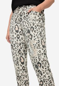 Pantalons léopard beiges avec des accents gris foncé et rose. Comprend une poche latérale et une illustration décorative de zèbre sur la cuisse.