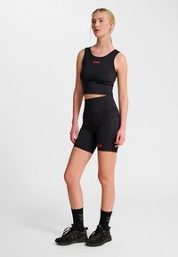 Svart sportig crop top och högmidjade shorts, båda med röda logotypdetaljer. Materialet verkar slätt och stretchigt; shortsen har fickor.