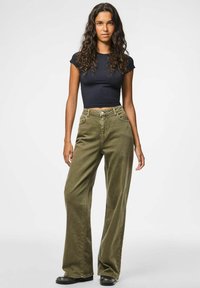 Olīvu zaļi, platā kāja bikses no kordūrām, ar augstu jostasvietu, ar priekšējiem kabatām un rāvējslēdzēju. Apvienotas ar pieguļošu melnu topu.