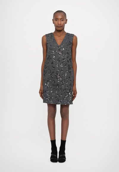 Vestido gris sin mangas con escote en V, adornado con lentejuelas en patrones florales; diseño hasta la rodilla combinado con calcetas y zapatos negros.