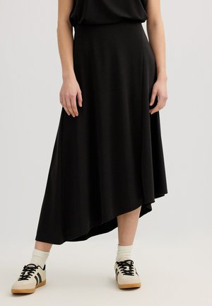 Mujer con falda midi asimétrica negra combinada con calcetines blancos y zapatillas beige con detalles en negro.