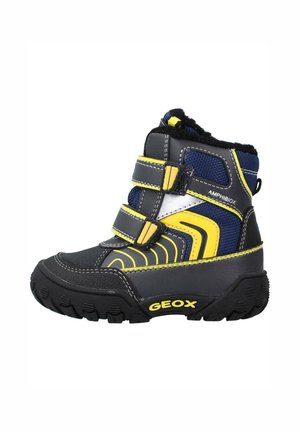 Bota de invierno para niños en negro, azul marino y amarillo con dos tiras de velcro, suela con dibujo grueso y forro polar etiquetado con "Amphibiox" y "Geox".