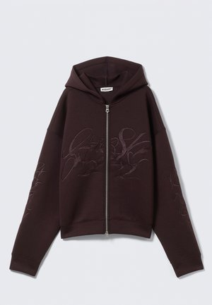 Haut à capuche zippé violet foncé avec une capuche ajustée, présentant des motifs brodés sur le devant et la manche, fabriqué en tissu doux et texturé.